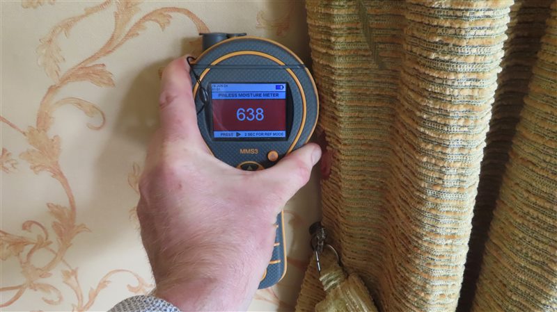 Surveyor taking an elevated moisture meter reading beside an internal wall